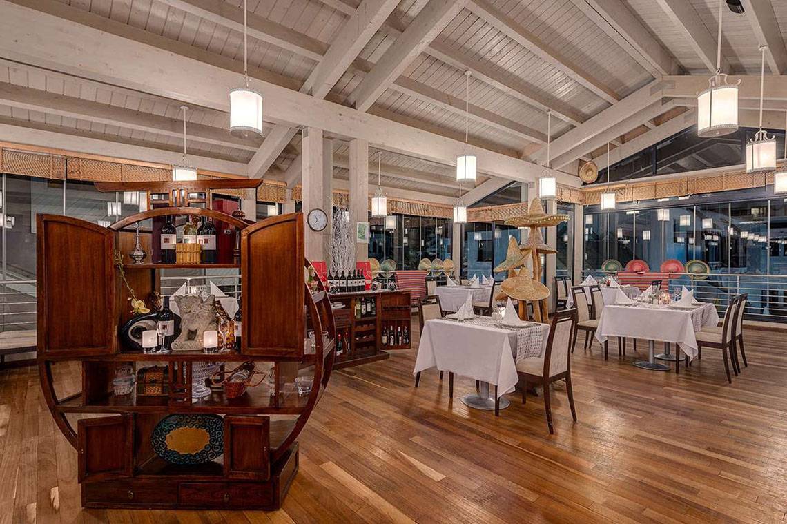 Innenansicht des Restaurants im Susesi Luxury Resort mit Holzboden, weißen Tischen und Stühlen.
