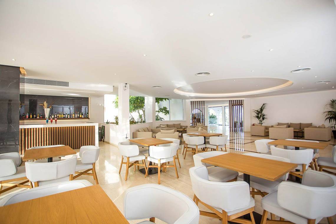 Loungebereich des Niriides Beach Hotels mit weißen Tischen und Stühlen.