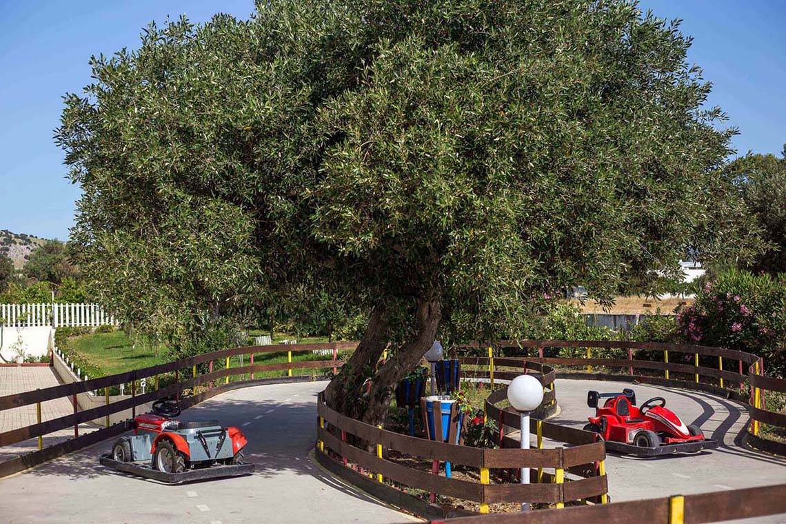 Zwei rote Go-Karts stehen auf der Rennstrecke des Niriides Beach Hotels neben einer großen Olivenbaum.