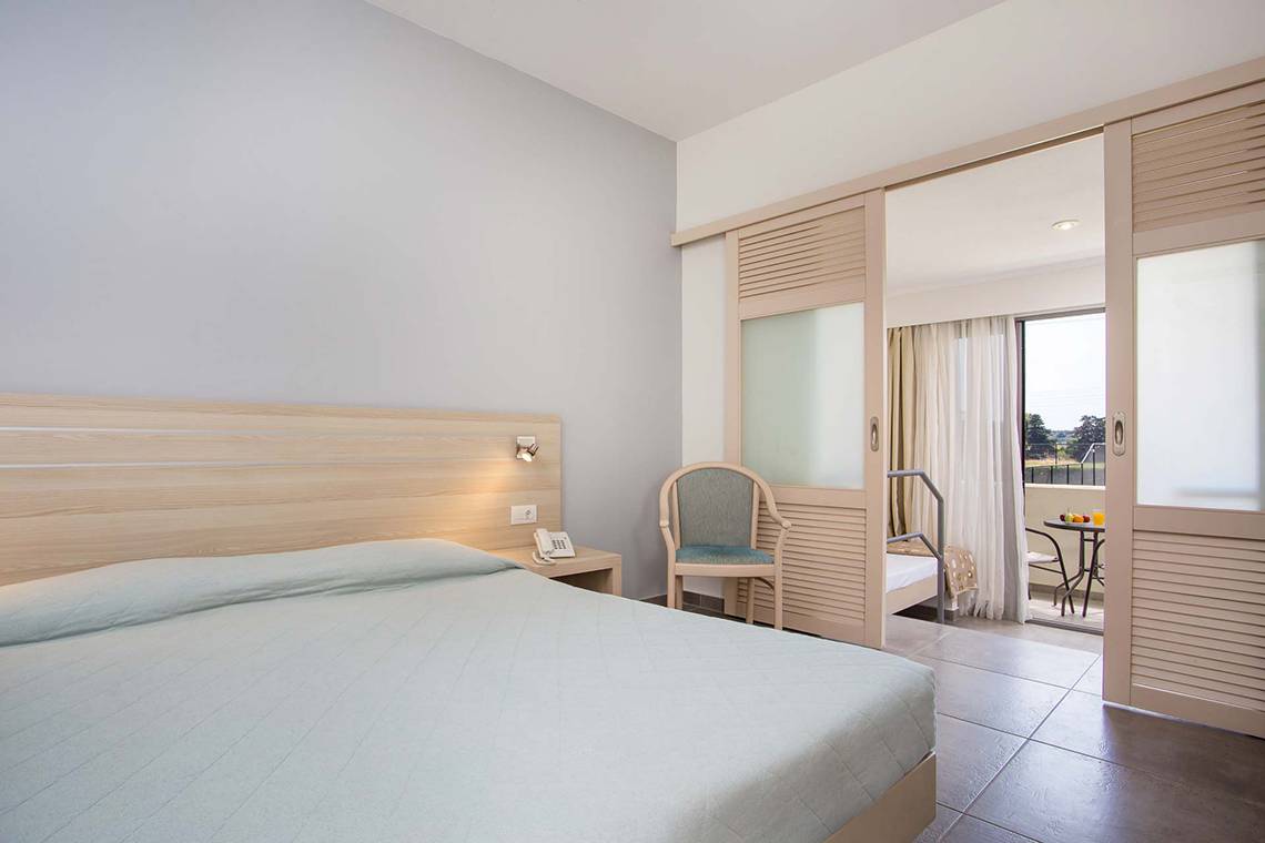 Innenansicht eines Hotelzimmers im Niriides Beach Hotel mit Bett, Stuhl und Balkon.