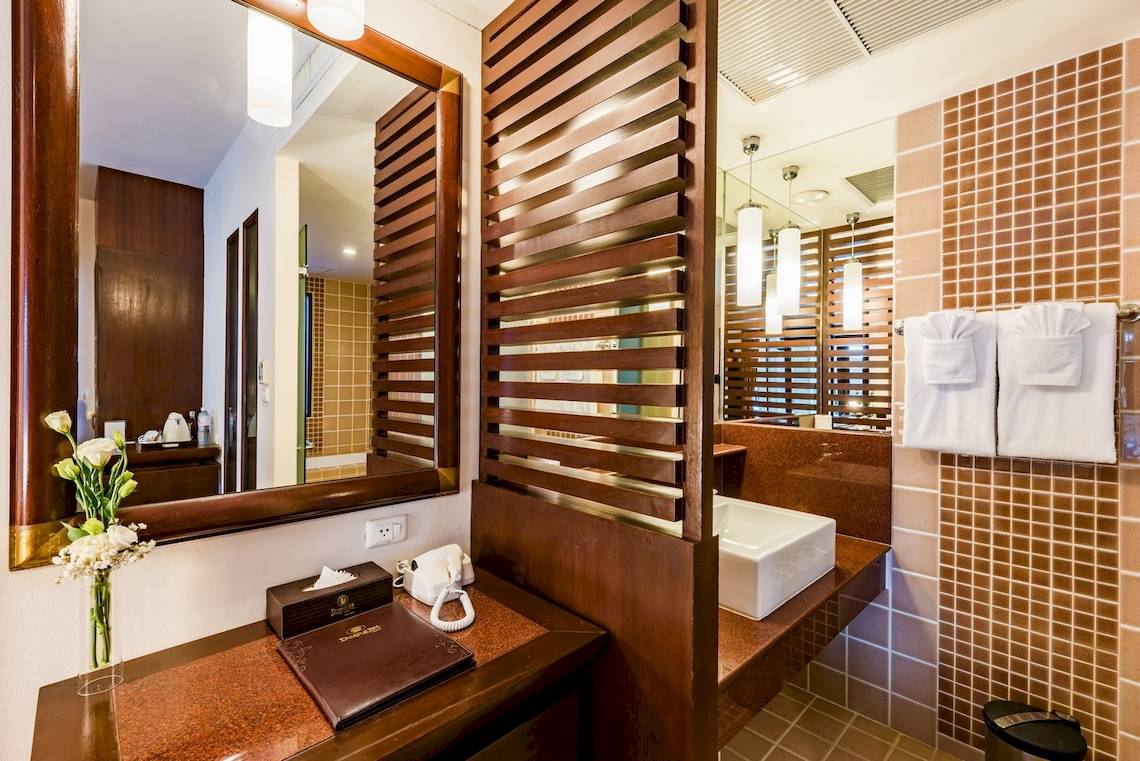 Badezimmer im Duangjitt Resort & Spa Hotel mit Spiegel, Blumenvase, Telefon und Waschbecken.