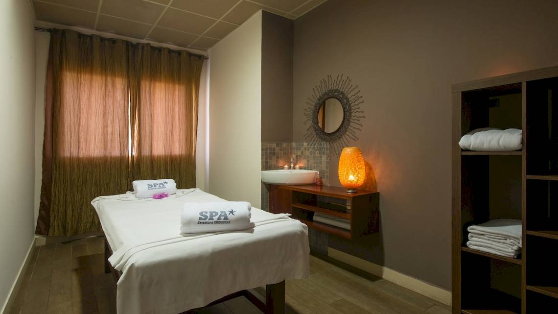 Spa-Behandlungsraum im VOI Praia De Chaves Resort mit einer Massageliege, einem Waschbecken, einem Spiegel und einer Lampe.