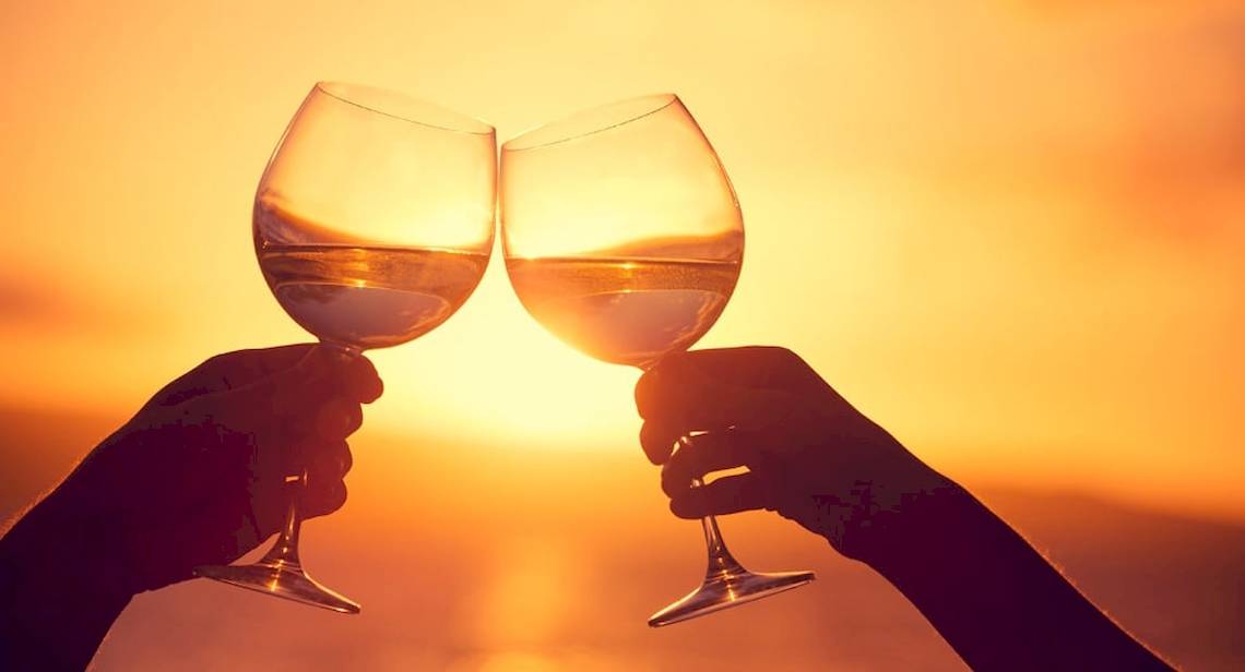 Zwei Personen stoßen mit Weingläsern bei Sonnenuntergang an.