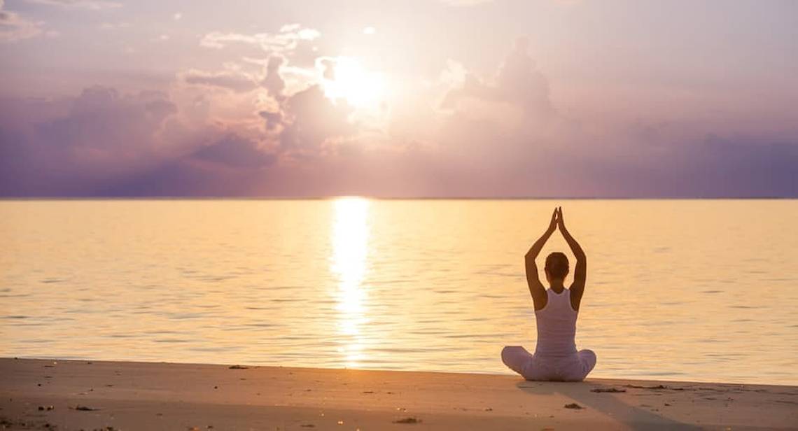Frau praktiziert Yoga auf dem Strand bei Sonnenuntergang