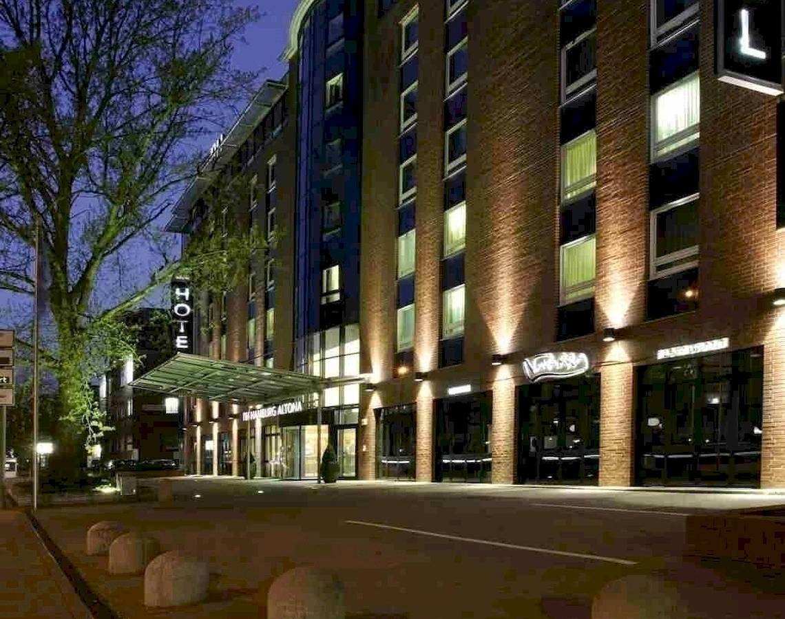 NH Hamburg Altona Hotel bei Nacht mit Beleuchtung und Bäumen vor dem Gebäude.