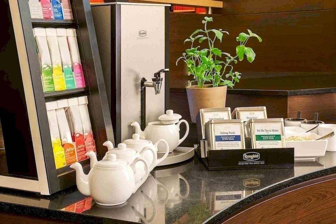 Getränkestation im NH Hamburg Altona Hotel mit Teekannen, Teebeuteln und Kräutertopf.