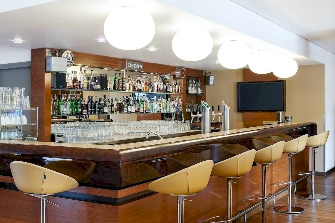 Barbereich im NH Hamburg Altona Hotel mit Barhockern, Theke und vielen Flaschen.