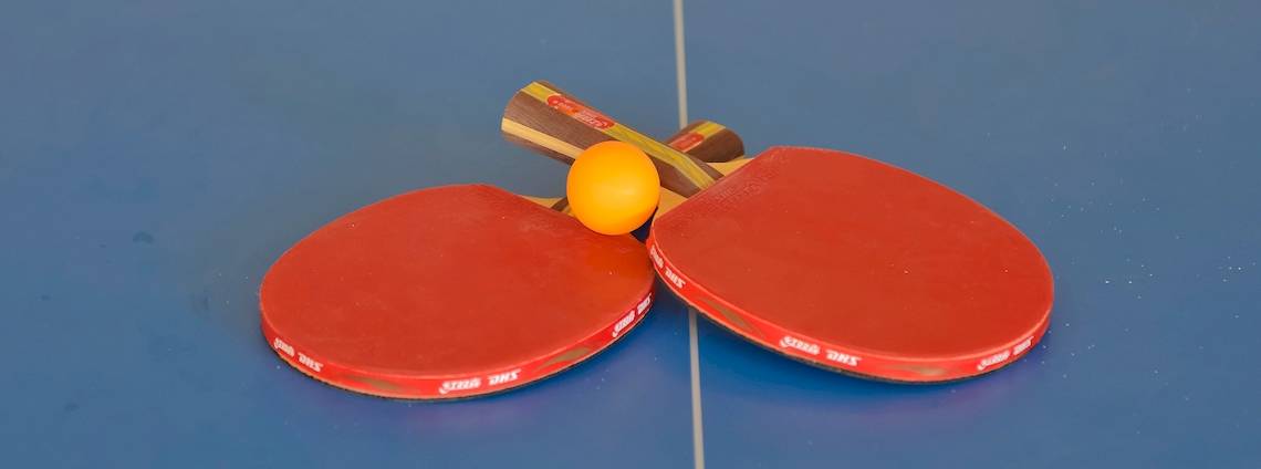 Zwei rote Tischtennisschläger mit einem gelben Ball auf einem blauen Tisch