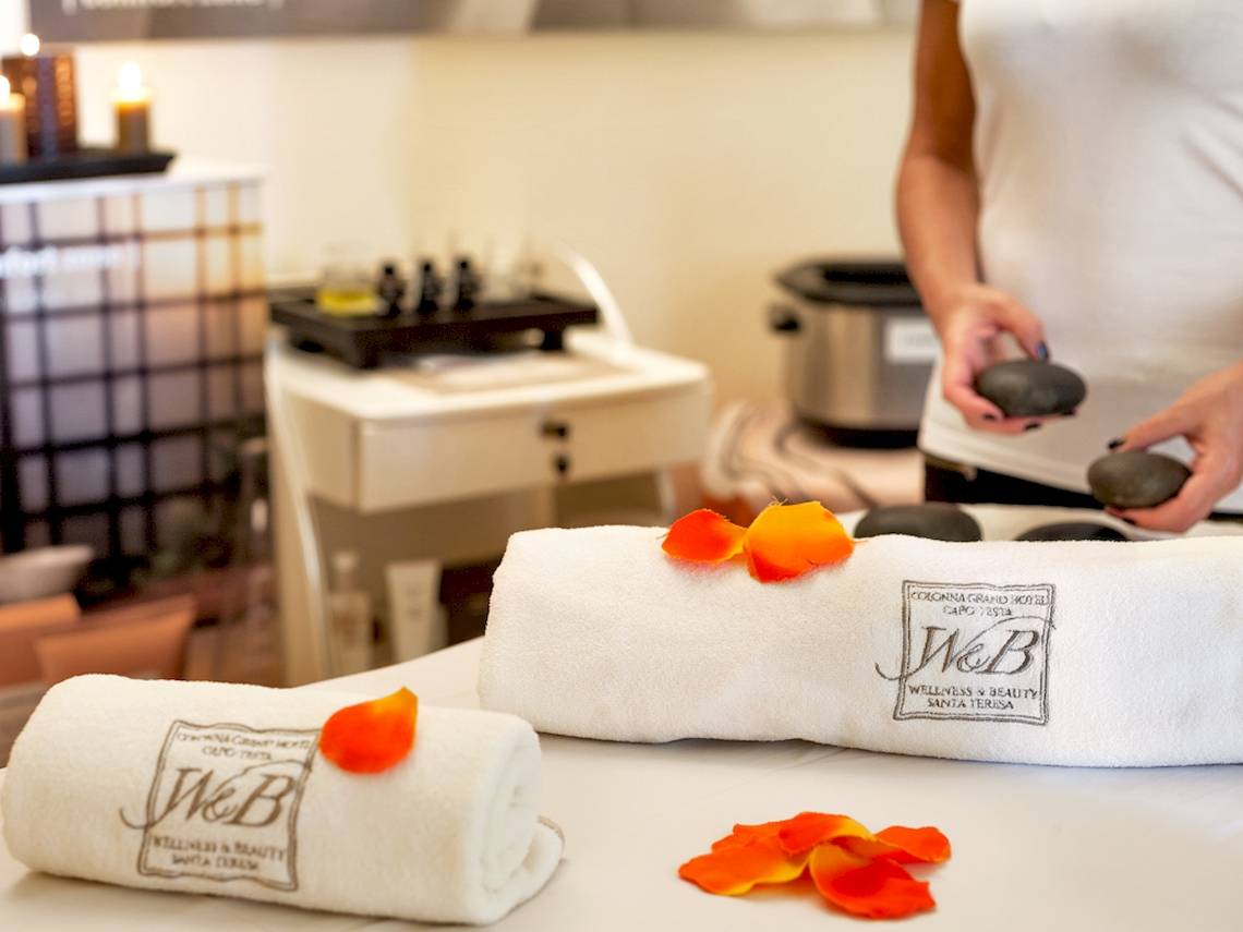 Spa-Behandlung im Colonna Grand Hotel Capo Testa mit weißen Handtüchern und Rosenblättern.
