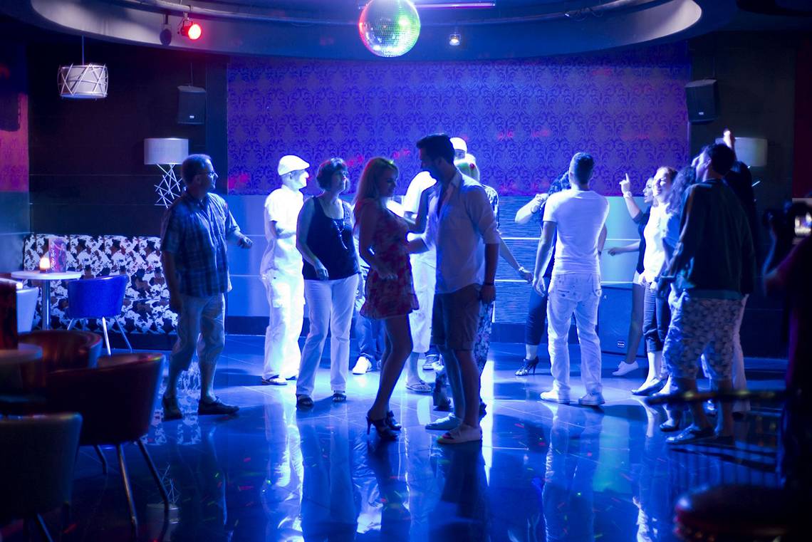 Menschen tanzen in einer Disco unter blauem Licht, mit einem Mann und einer Frau, die sich umarmen.