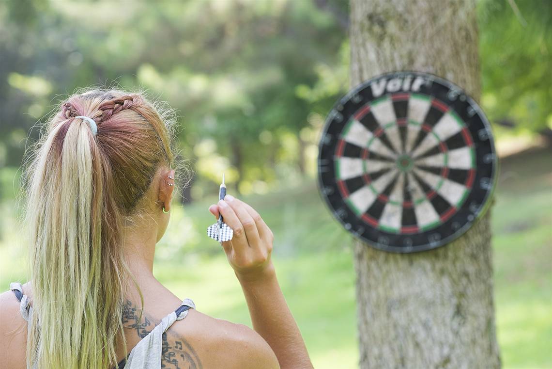 Frau wirft Dart auf eine Scheibe, die an einem Baum befestigt ist.