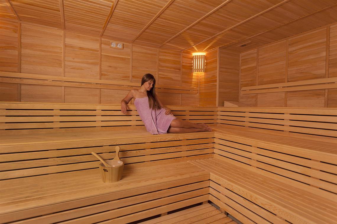 Eine Frau in einem rosa Handtuch sitzt in einem Holzsaunabereich des Club Hotel Sidelya.