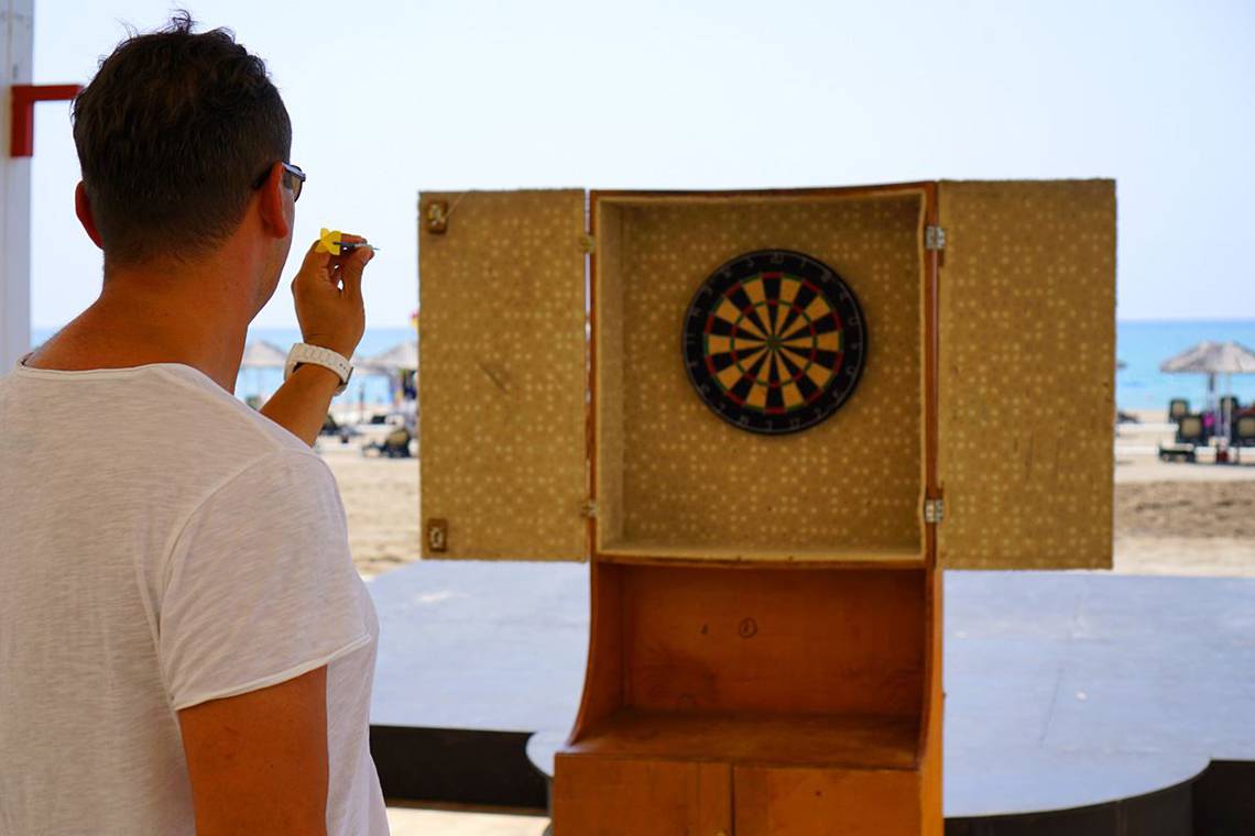 Mann wirft Pfeil auf eine Dartscheibe auf dem Strand.