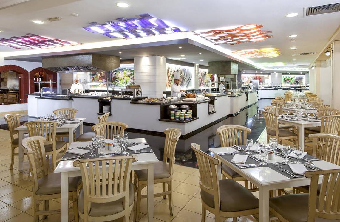 Innenansicht des Restaurants im Sol Palmeras Hotel mit gedeckten Tischen und Köchen hinter der Theke.