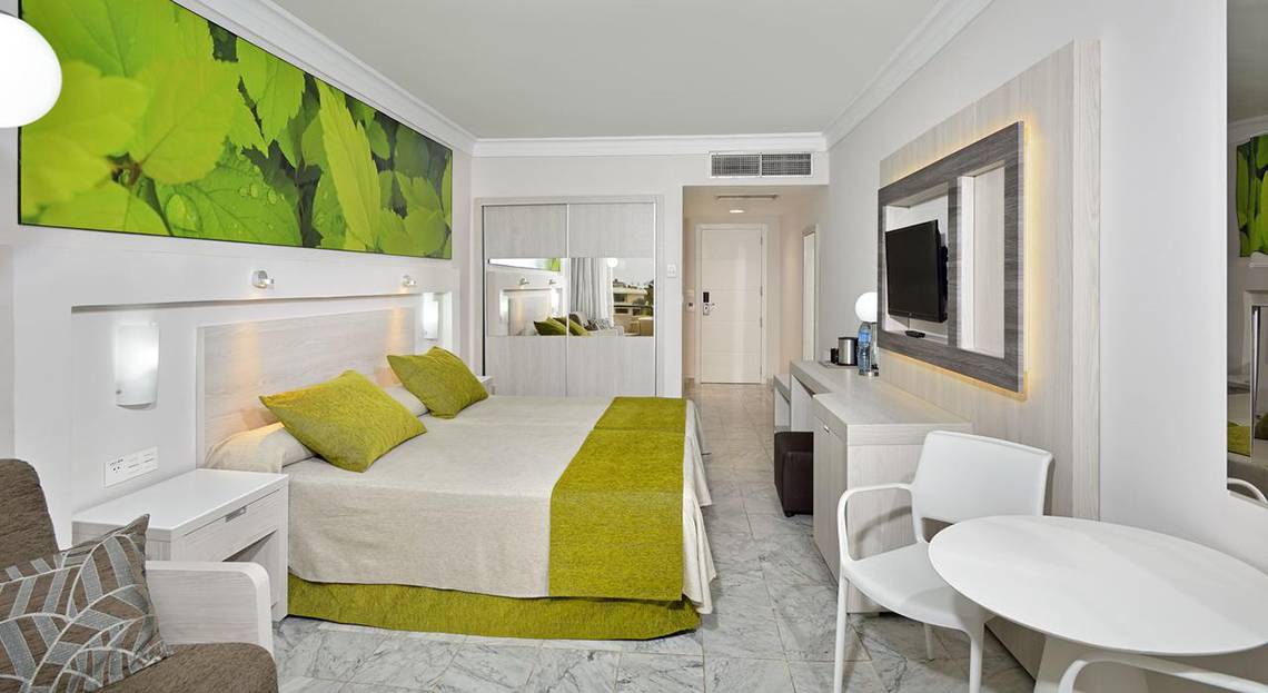 Innenansicht eines Hotelzimmers im Sol Palmeras Hotel mit grünem Bett und weißen Möbeln.