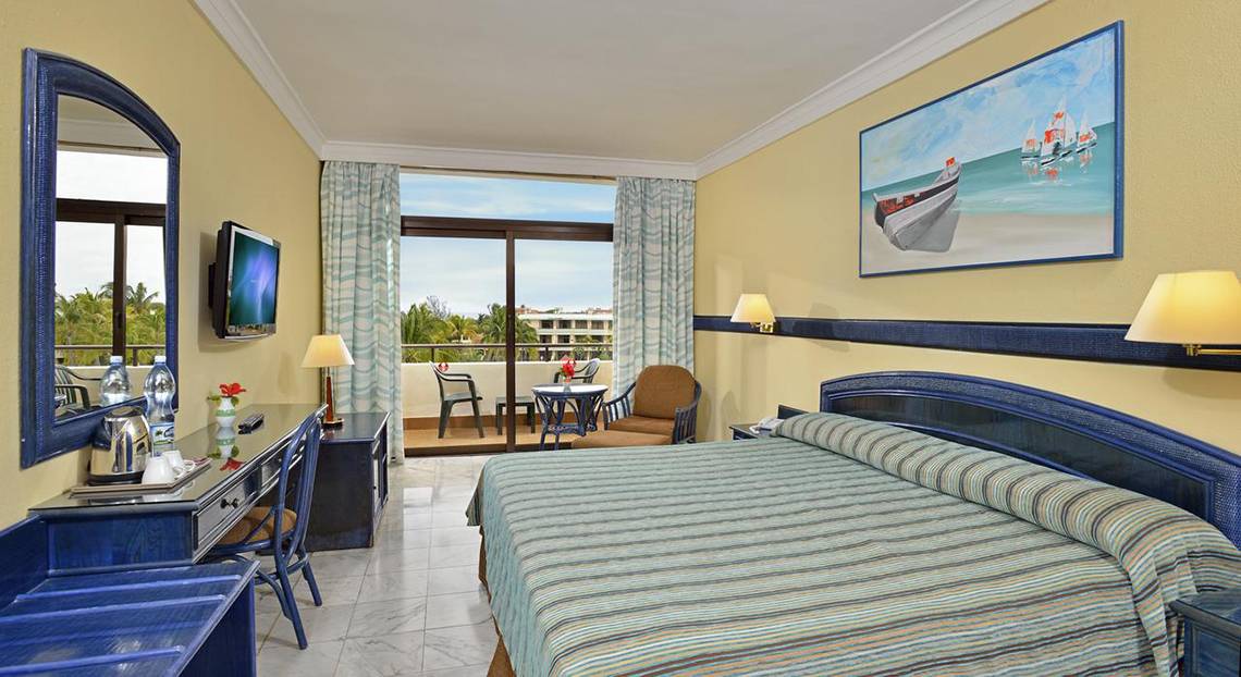 Innenansicht eines Hotelzimmers im Sol Palmeras Hotel mit Balkon, Fernseher, Schreibtisch und Gemälde.