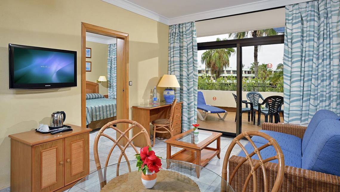 Innenansicht des Sol Palmeras Hotelzimmers mit Fernseher, Schreibtisch, Loungebereich und Balkon.