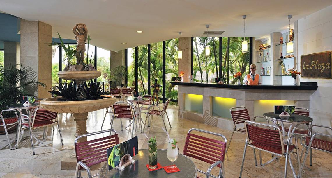 Innenansicht der Lobby-Bar des Sol Palmeras Hotels mit Brunnen, Tischen, Stühlen und einer Barfrau.