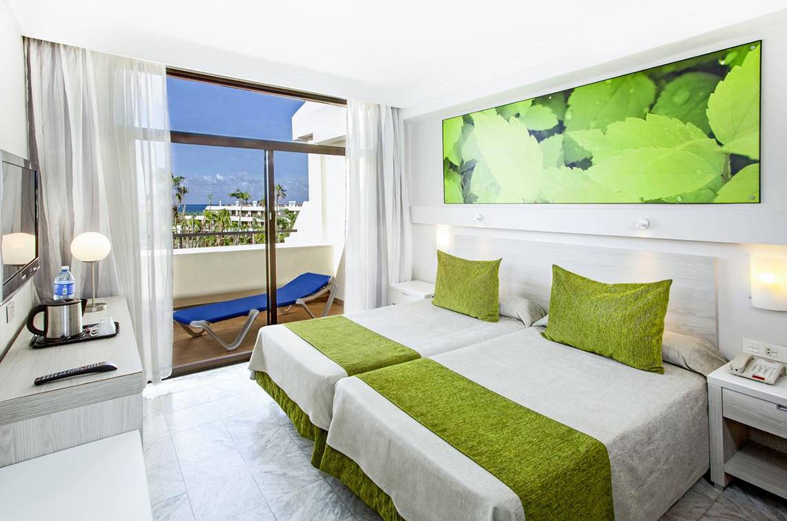 Doppelzimmer im Sol Palmeras Hotel mit zwei Betten, grünen Kissen und einem Balkon.