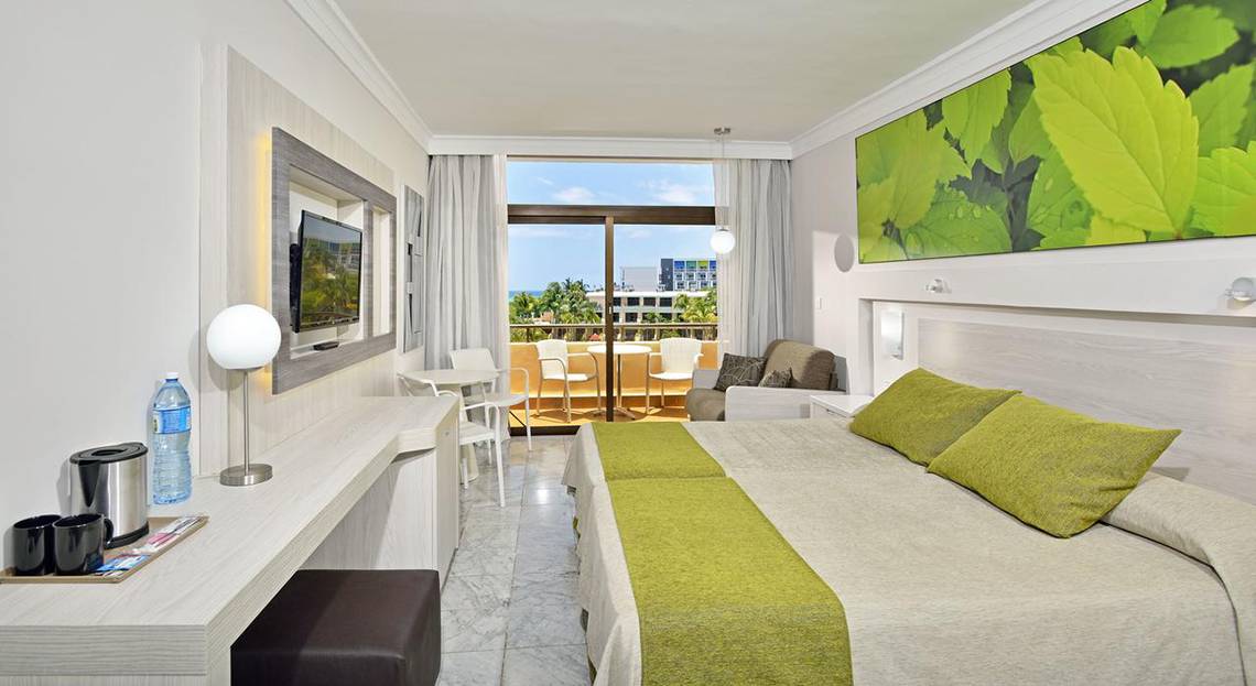 Hotelzimmer im Sol Palmeras mit zwei Betten, Schreibtisch, Fernseher und Balkon mit Meerblick.