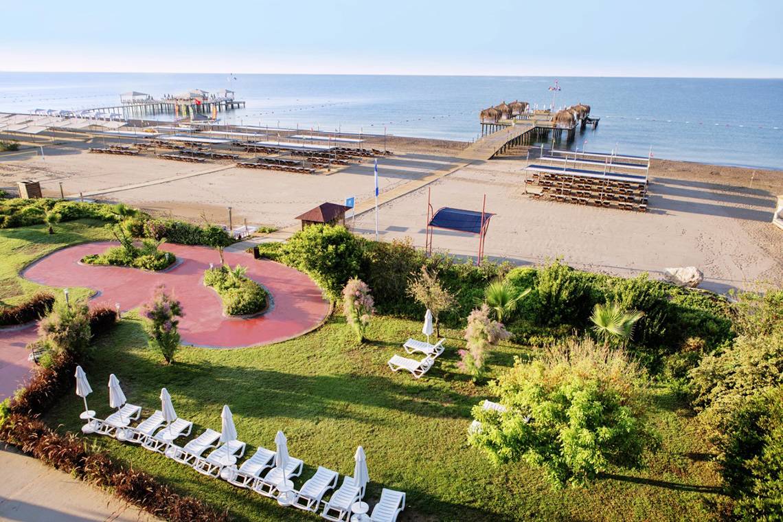 Luftaufnahme des Liberty Hotels Lara am Strand mit Sonnenliegen, Pflanzen und einem Steg.