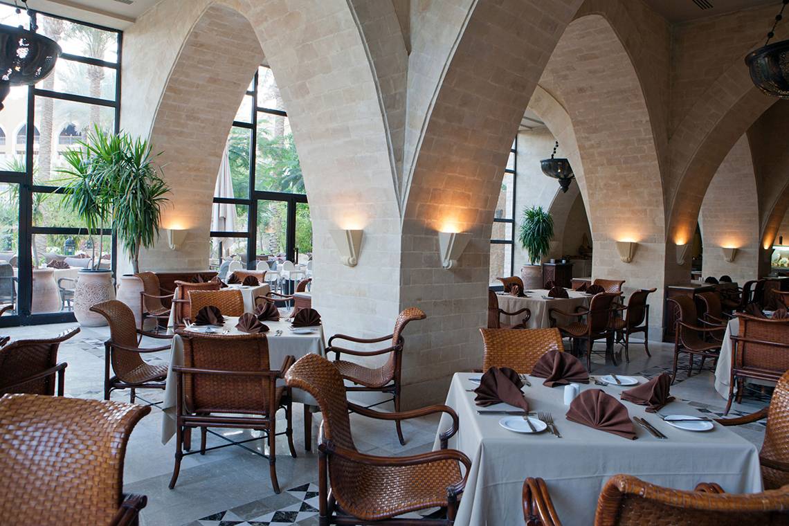 Restaurant im Grand Waterworld Makadi Hotel mit braunen Stühlen und Tischen, gerahmt von hohen Bögen.