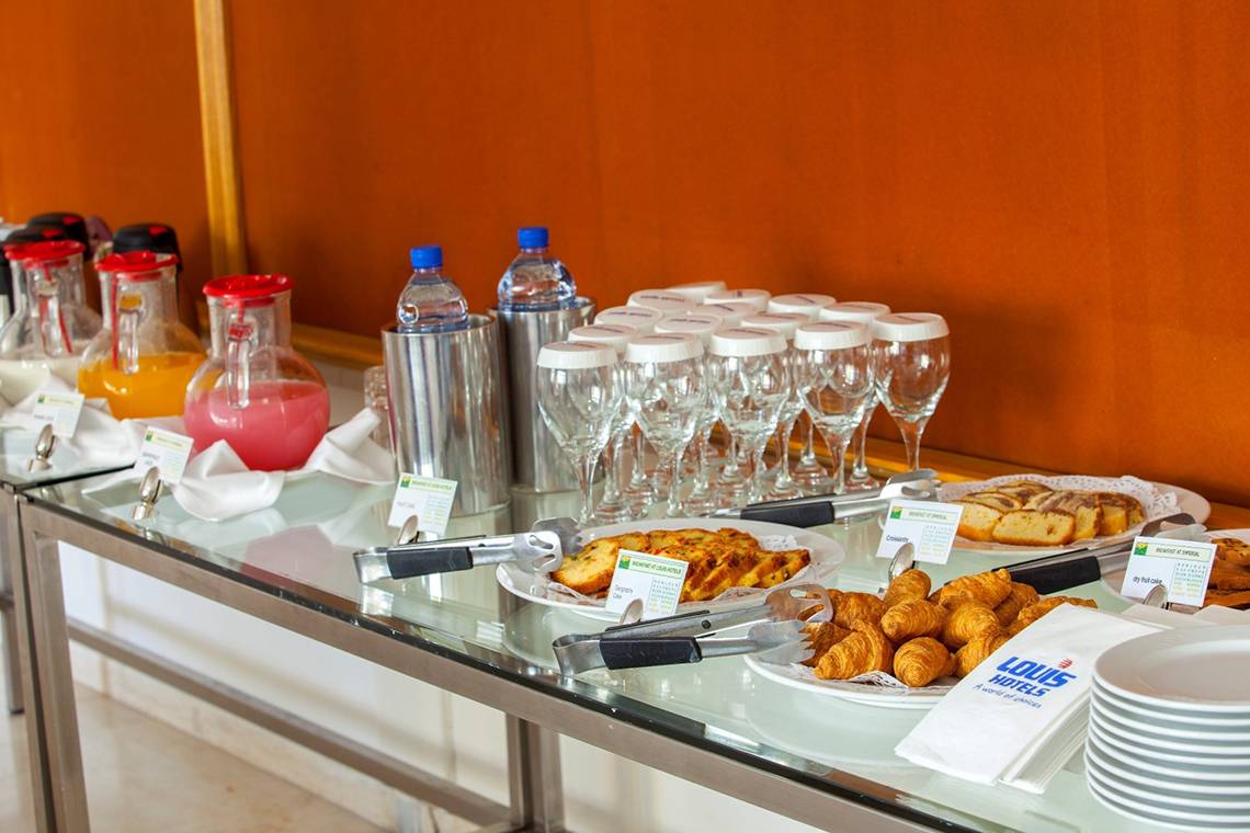Frühstücksbuffet im Louis Imperial Beach Hotel mit Croissants, Brötchen, Säften und Wasserflaschen.