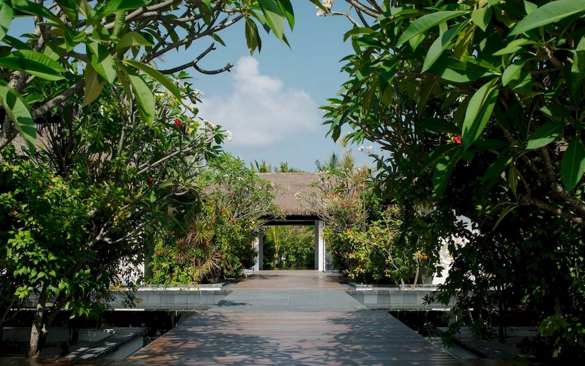 Eingang des Noku Maldives Hotels umgeben von tropischen Pflanzen und Bäumen.