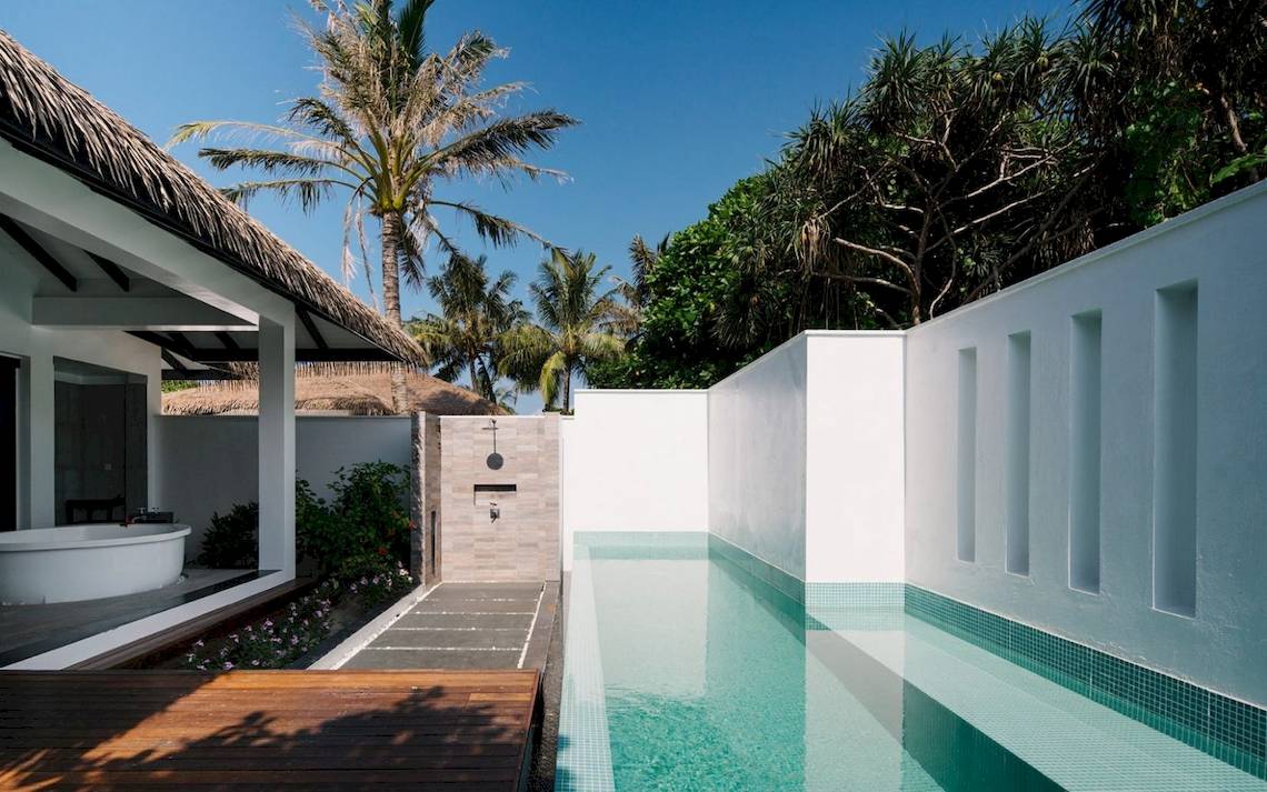 Außenpool und Badewanne im Noku Maldives Hotel, umgeben von Palmen und Pflanzen.