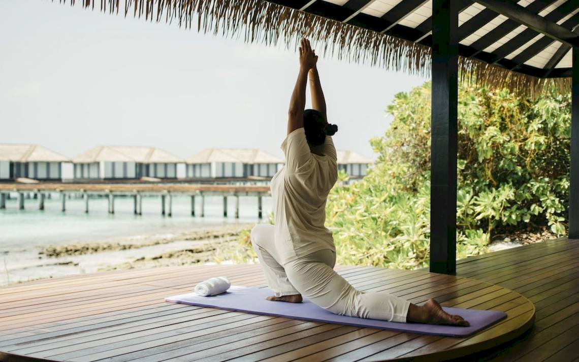 Frau macht Yoga auf einem Holzdeck im Noku Maldives.