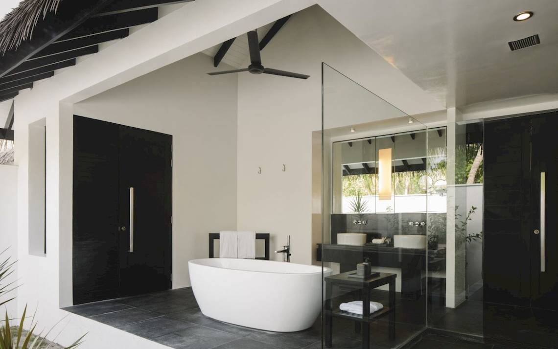 Badezimmer im Noku Maldives Hotel mit Badewanne, Glasdusche und schwarzen Türen.