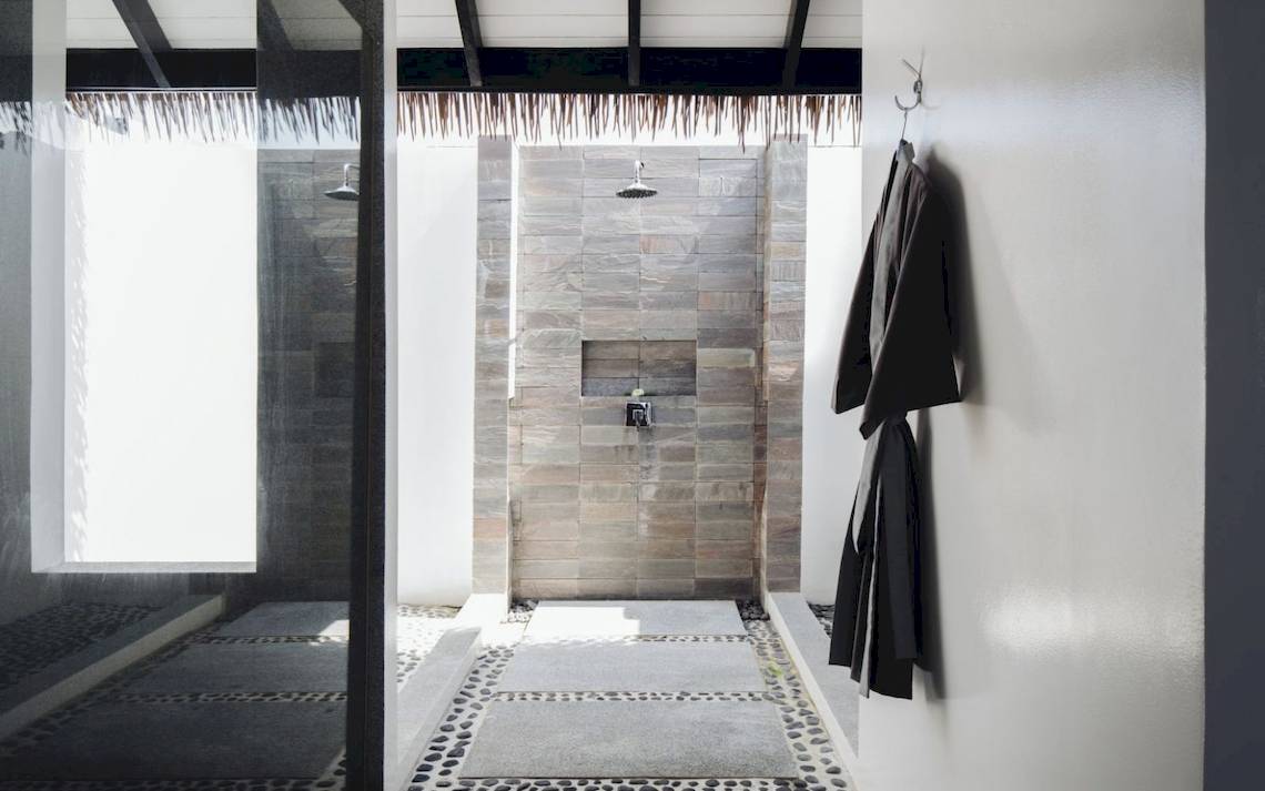 Dusche im Noku Maldives Hotel mit steinerner Wand und offenem Eingang.