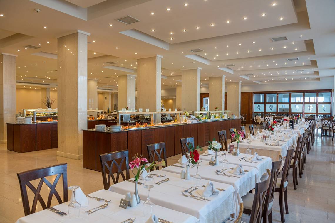 Innenansicht des Kresten Palace Restaurants mit langen, gedeckten Tischen und einer Theke im Hintergrund.