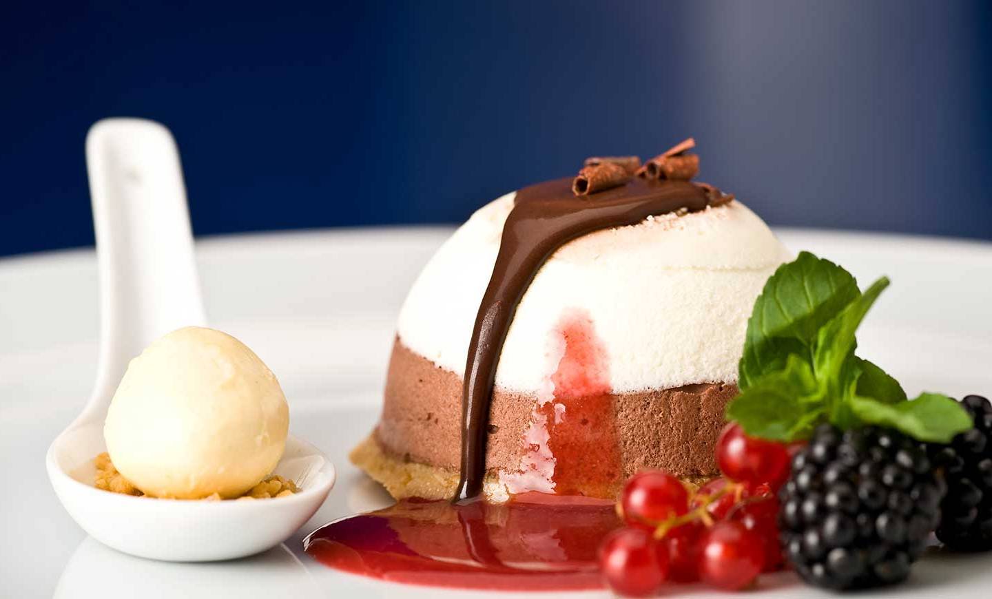 Ein Dessert mit Schokoladencreme, Beeren und Sahne auf einem weißen Teller.