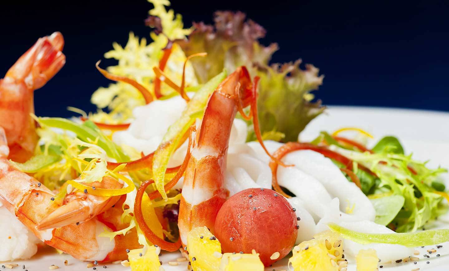 Nahaufnahme von Garnelen und Salat auf einem weißen Teller mit einer blauen Hintergrund.