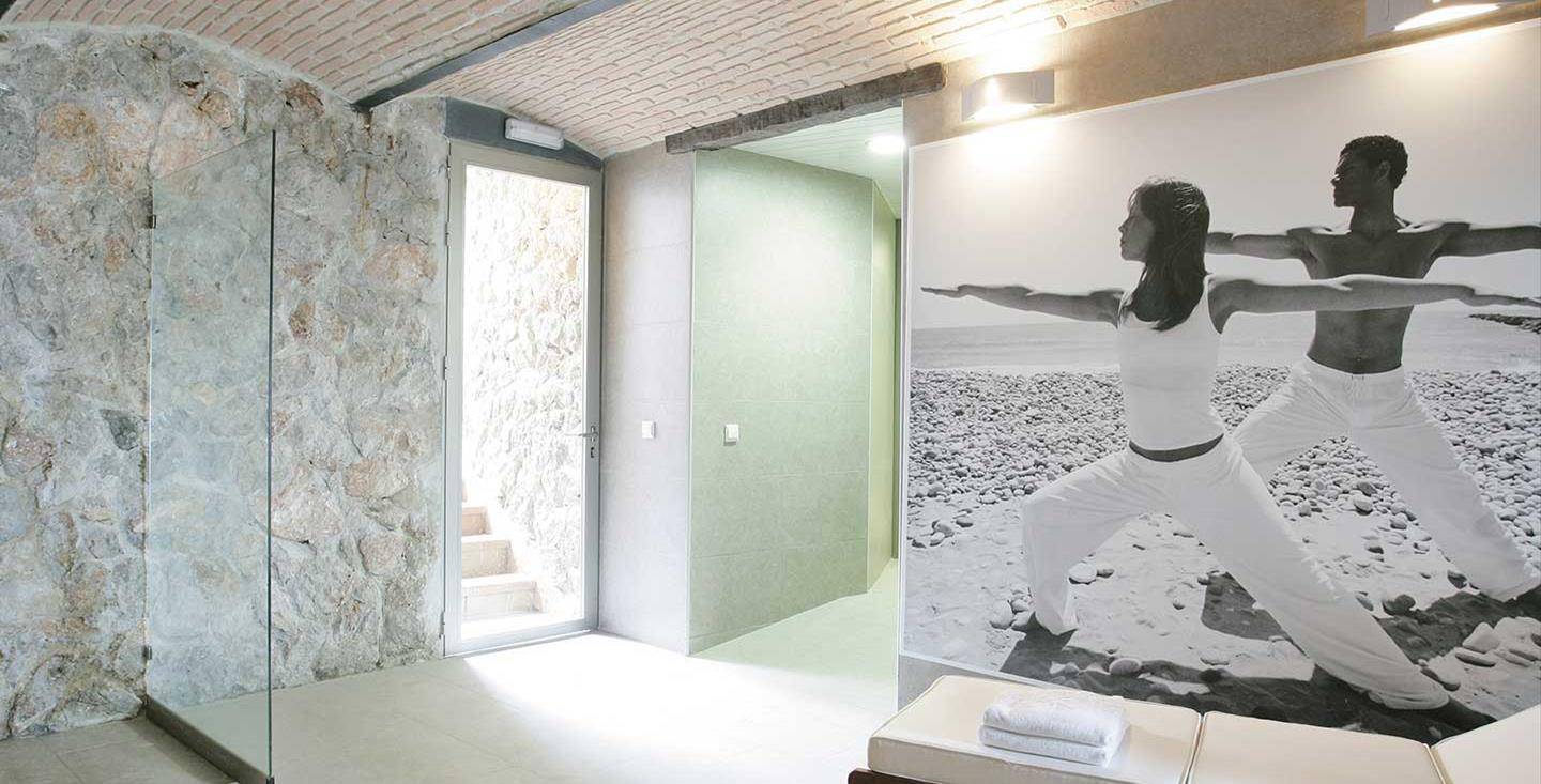 Innenansicht eines Yoga-Raums im Barcelo Illetas Albatros Hotel mit einer Steinwand und einem Foto von zwei Menschen in Yoga-Pose.