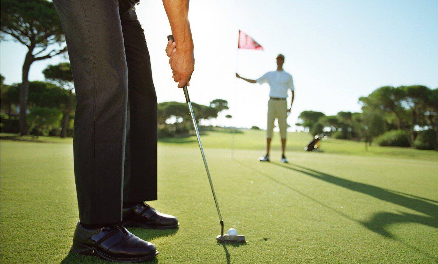 Golfer puttet auf dem Golfplatz mit einem Caddie im Hintergrund.