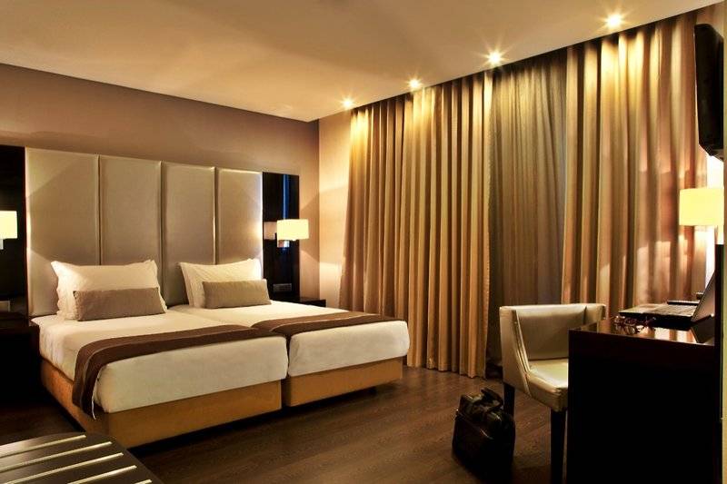 Doppelbettzimmer im Turim AV Liberdade Hotel mit goldenen Vorhängen und Schreibtisch.