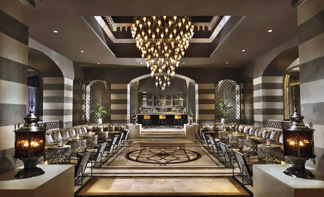 Innenansicht des Restaurants im Steigenberger Alcazar Hotel mit gemusterten Wänden, einem großen Kronleuchter und Sitzbereichen.