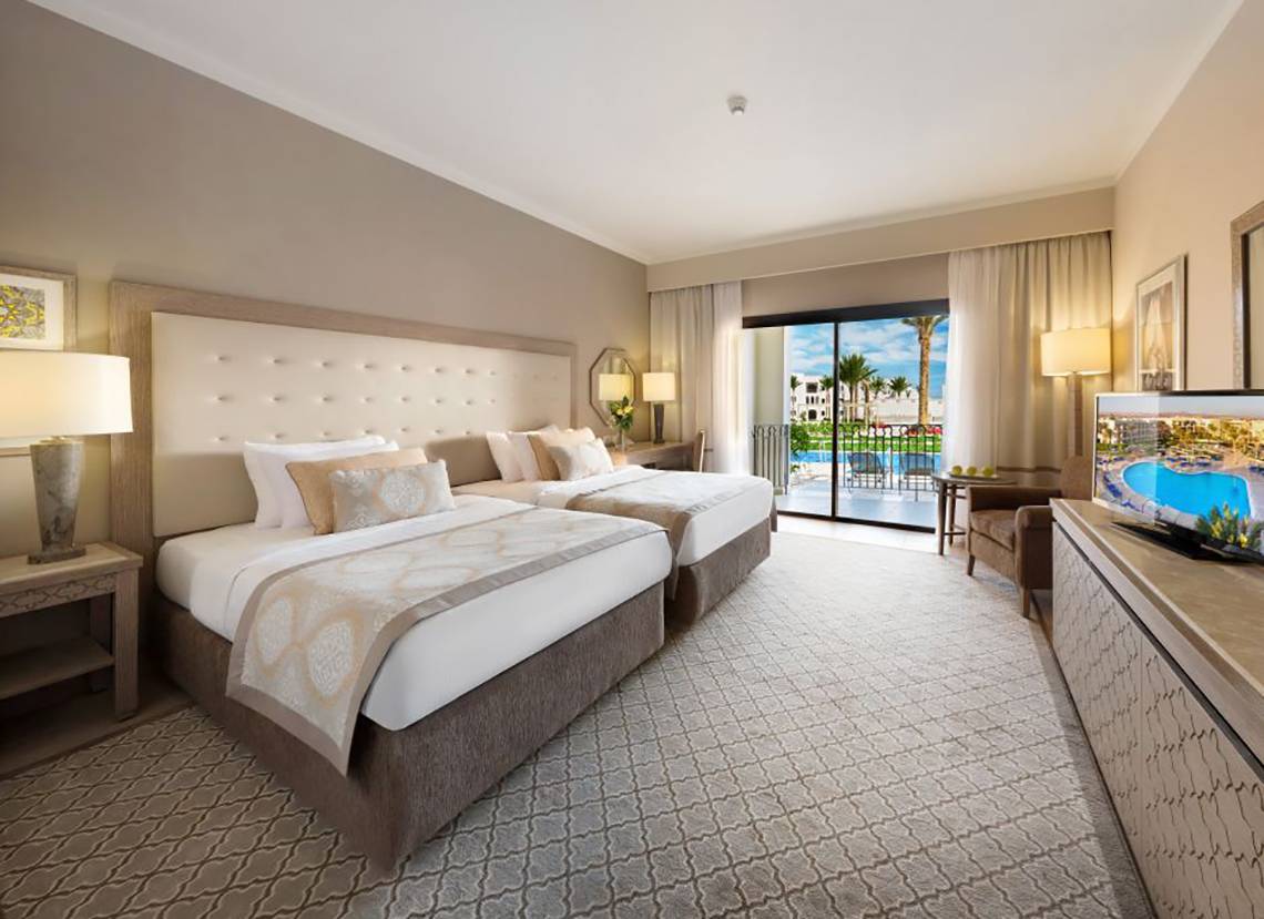 Doppelzimmer im Steigenberger Alcazar mit zwei Betten, Fernseher, und Balkon mit Poolblick.