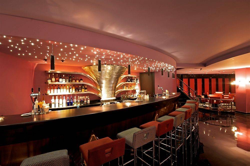 Innenansicht der Bar im Iberostar Grand Rose Hall Hotel mit voll ausgestatteter Theke und roten Barhockern.