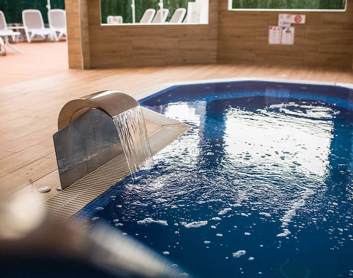 Ein Innenpool des Servatur Waikiki Hotels mit Wasserfall und blauem Wasser.