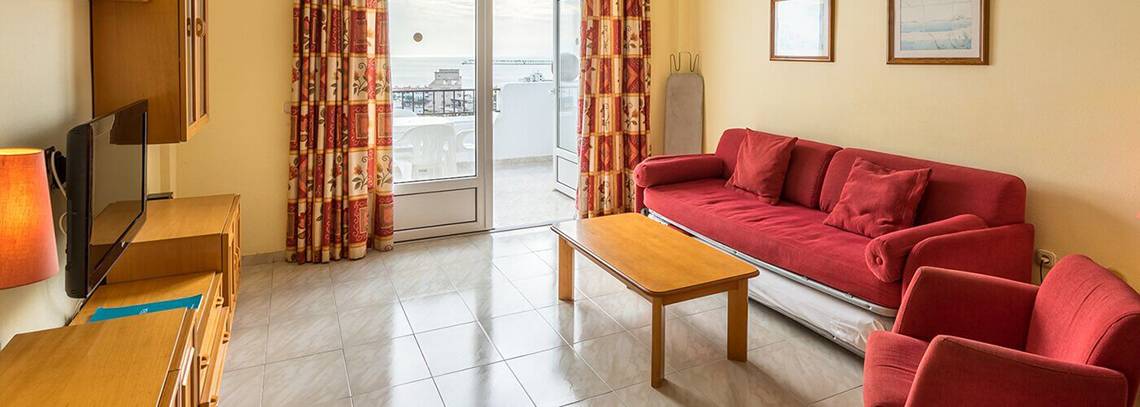 Wohnzimmer im Bluesea Callao Garden Hotel mit rotem Sofa, Couchtisch und Fernseher.
