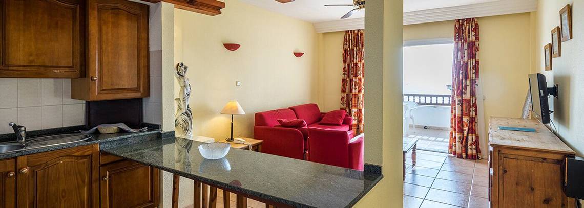 Wohnbereich des Bluesea Callao Garden Hotels mit Küchenzeile, rotem Sofa und Fernseher.