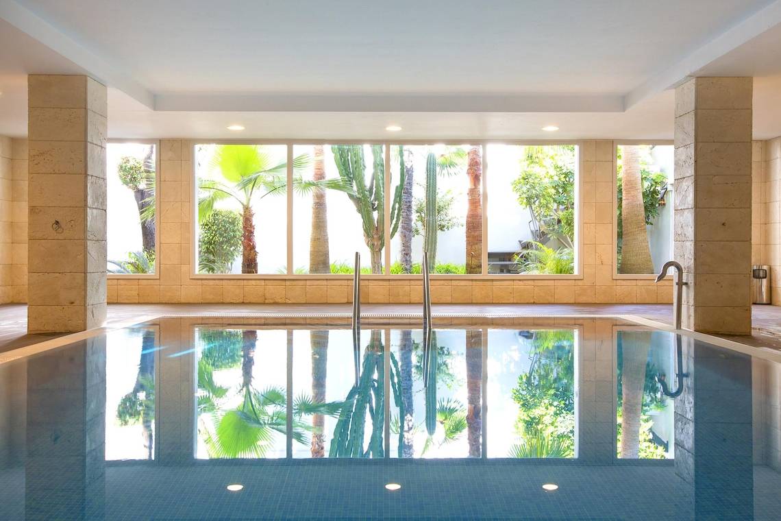 Innenansicht des Swimmingpools im Hipotels Hipocampo Playa Hotel mit großen Fenstern und tropischen Pflanzen.