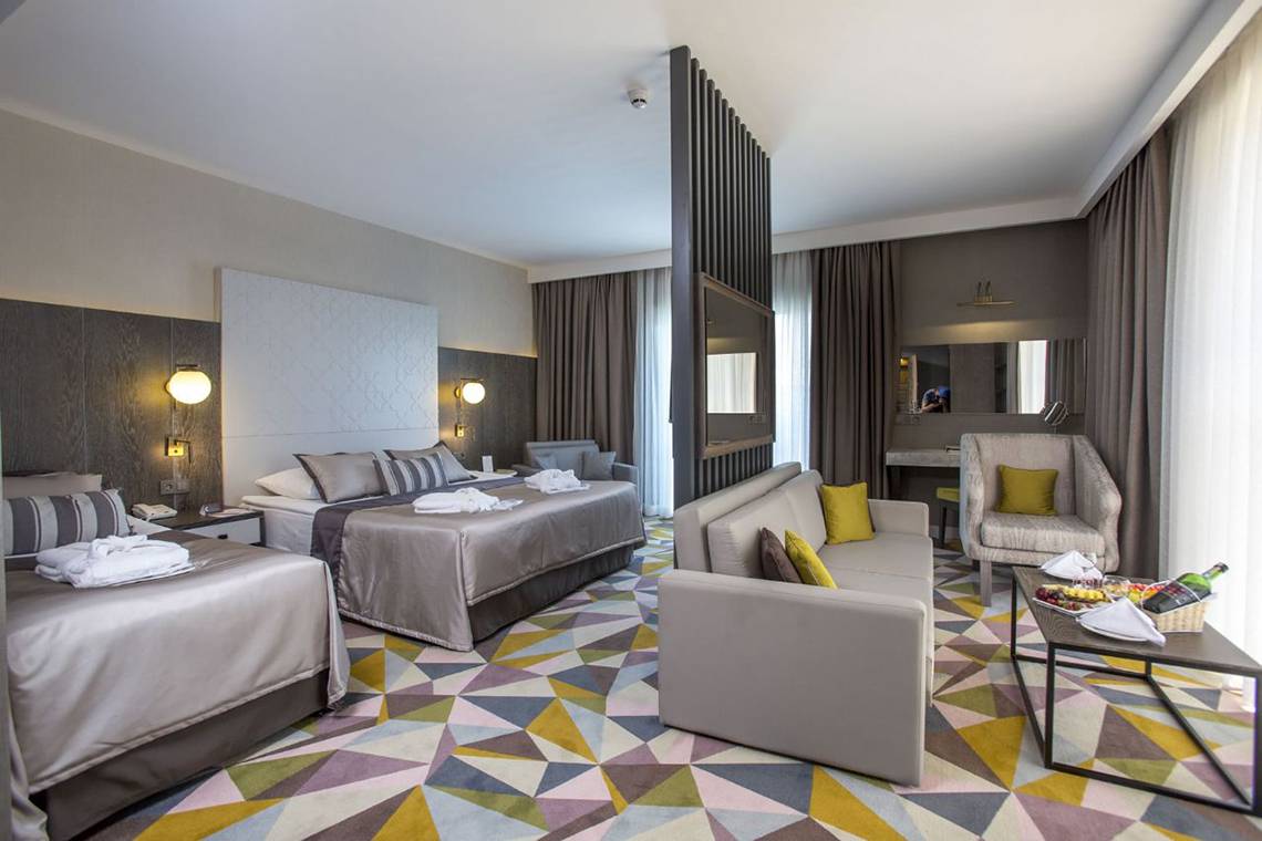 Suite-Innenansicht im Fame Residence Lara & Spa mit zwei Betten, Couch, Tisch und Teppichboden.