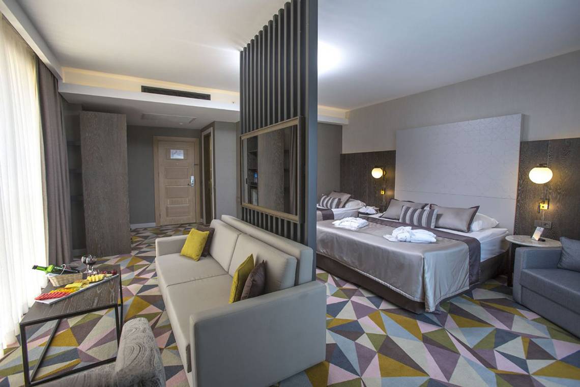 Suite-Schlafzimmer im Fame Residence Lara Hotel mit zwei Betten, Sofa und Esstisch.