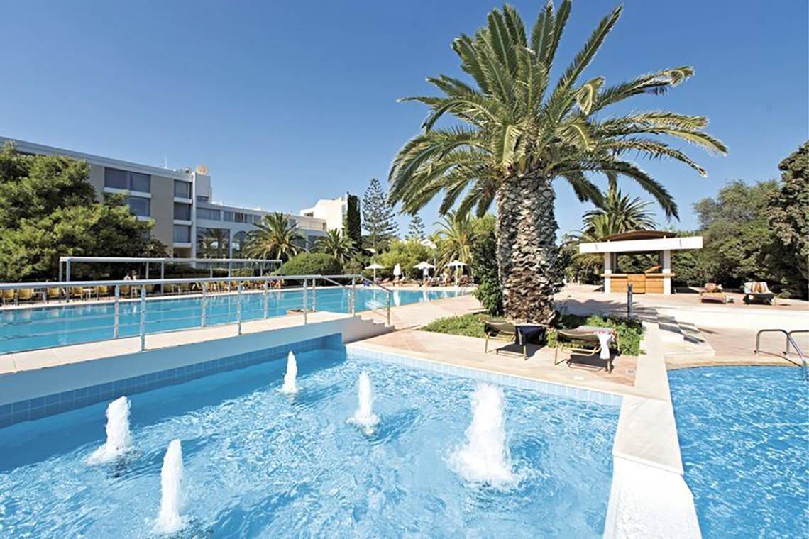 Außenbereich des Caravia Beach Hotel mit Swimmingpool und Palme.