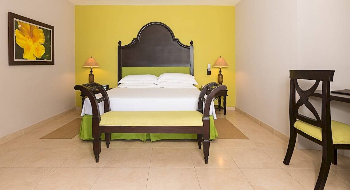 Ein farbenfrohes Schlafzimmer im Occidental Papagayo Hotel mit gelben Wänden, einem großen Bett und Nachttischen.