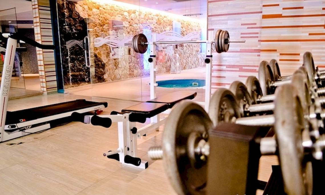 Fitnessbereich im La Mer Deluxe Hotel & Spa mit Laufband, Hantelbank und freien Hanteln.